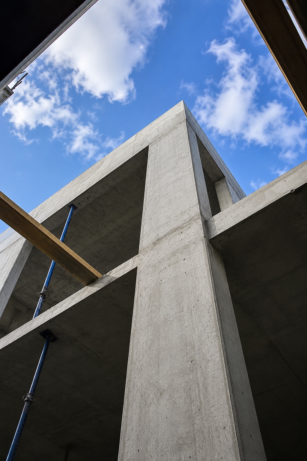 Upward view of a concrete structure under construction against a blue sky with clouds